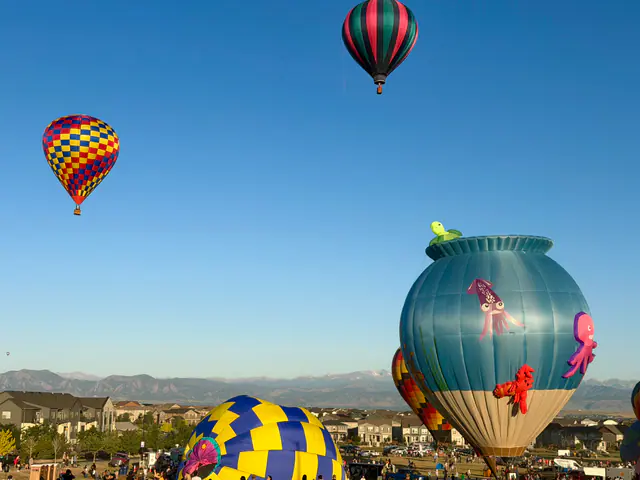 Colorful hot-air balloons rise above a festival field beneath a clear blue sky