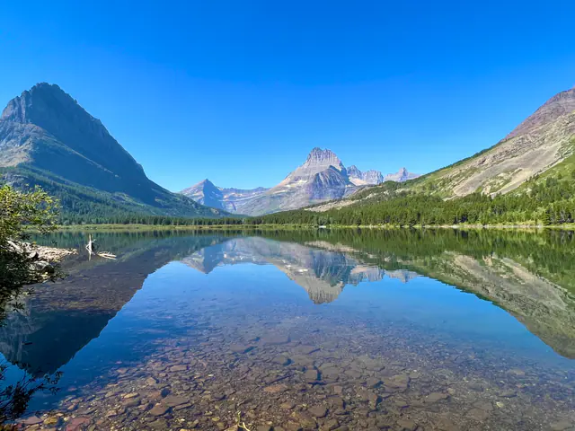 A glassy mountain lake reflects steep peaks beneath a vivid blue sky