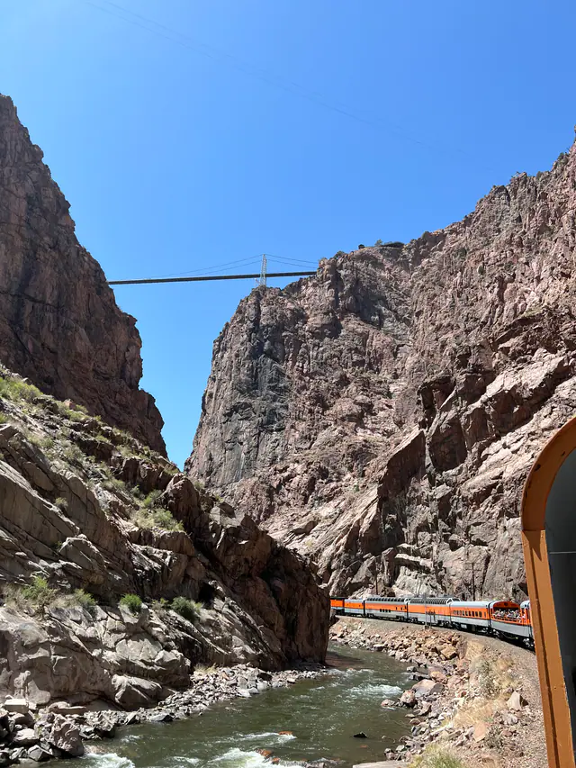 A narrow suspension bridge spans a steep rocky mountain canyon