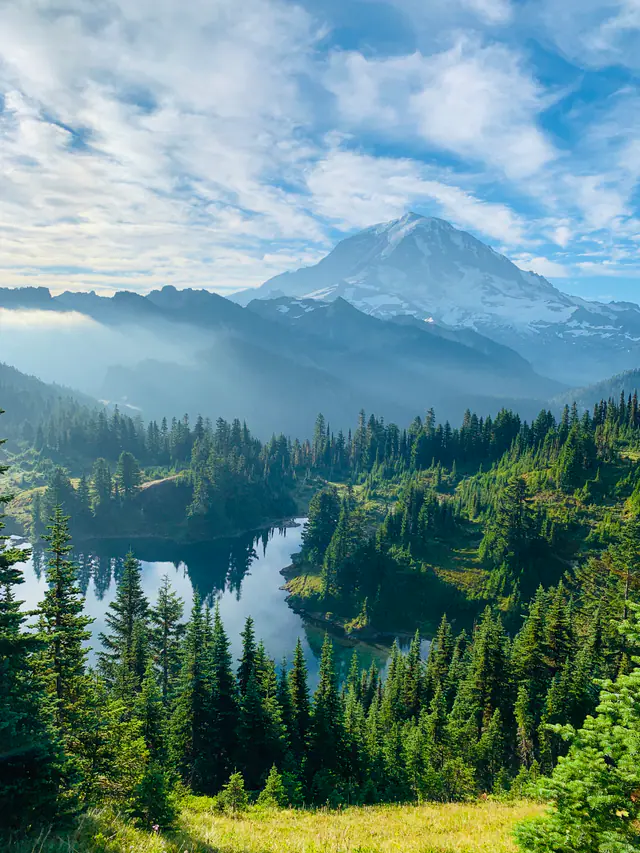 A distant volcanic peak rises above forested ridges and low clouds