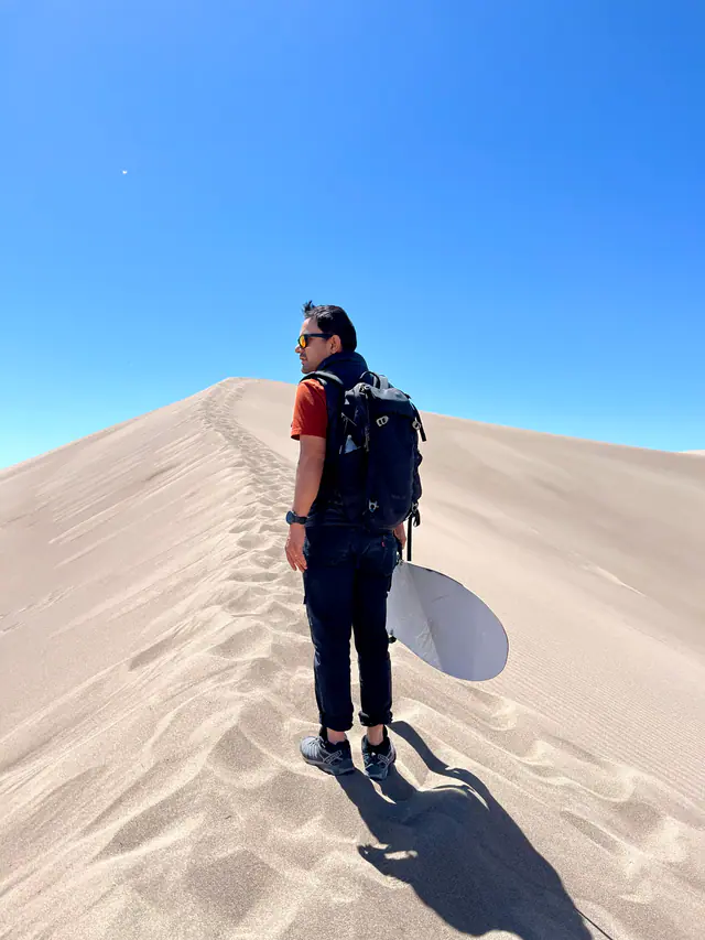 A person carrying a sled walks across rippled white sand dunes