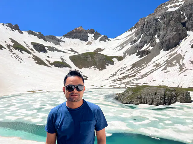 Nitesh stands in front of a partly frozen turquoise alpine lake