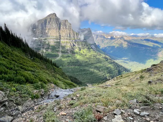A trail descends through a broad green valley between layered mountain walls