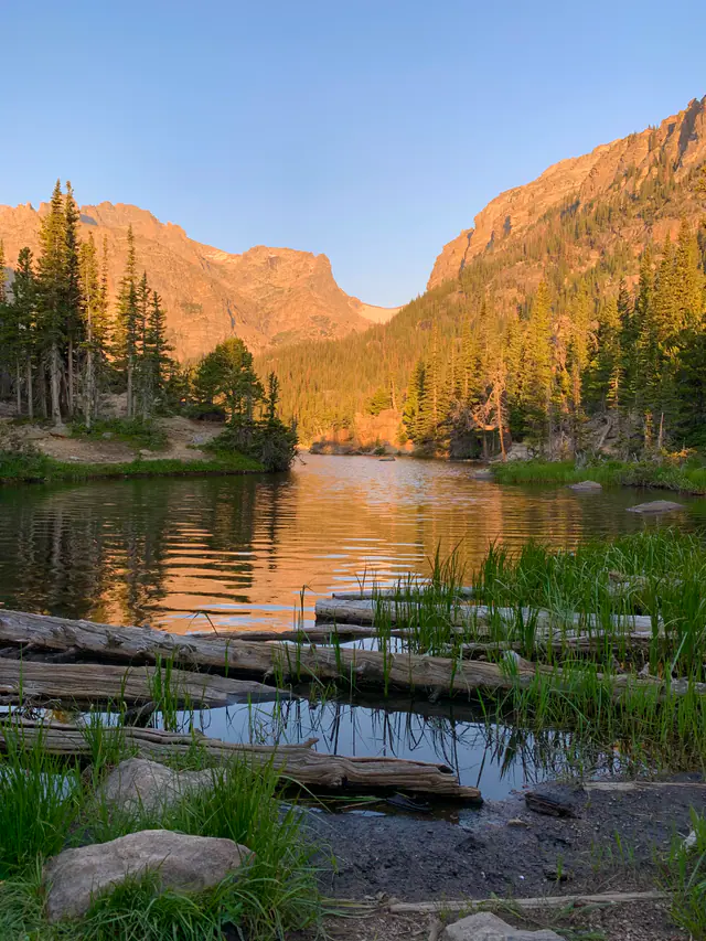 A calm mountain lake glows in warm evening light beneath an orange ridge