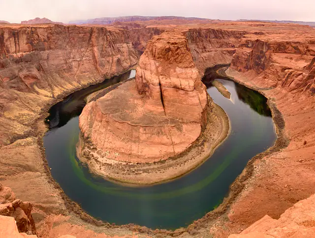 A horseshoe-shaped river curves around a massive red sandstone formation