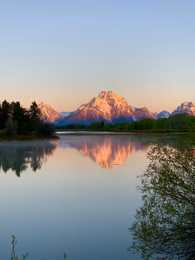 Pink sunrise light touches a rugged mountain reflected in a still river