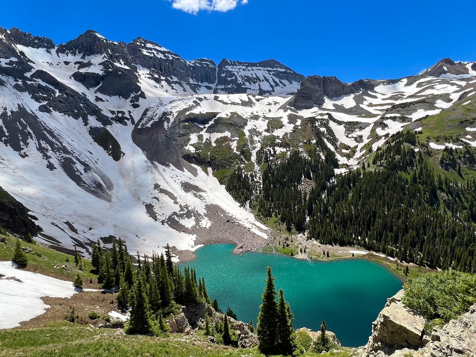 A turquoise alpine lake beneath a snow-striped mountain basin