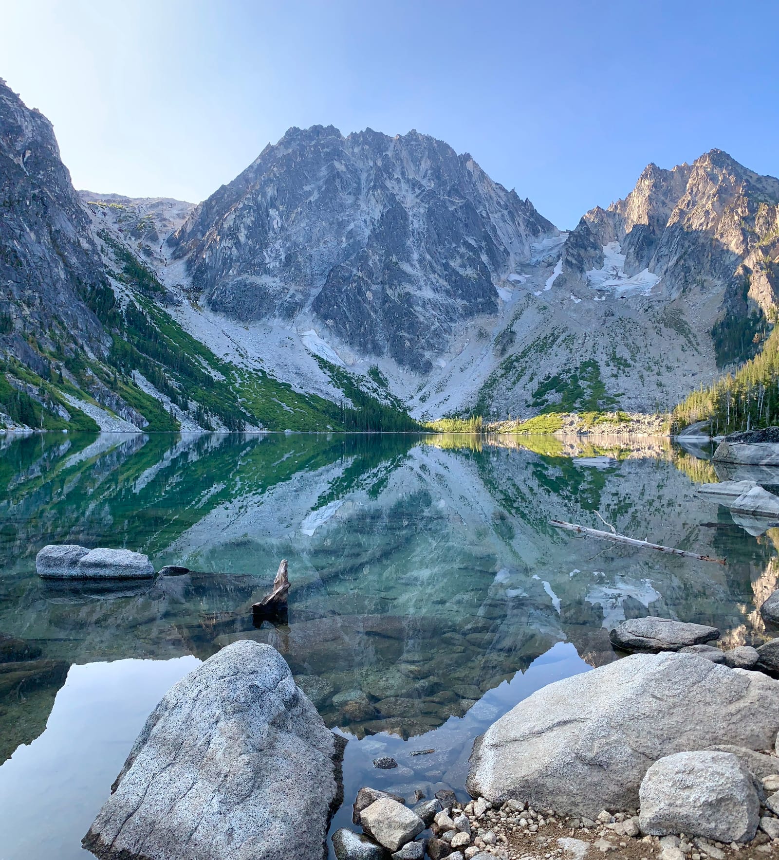 A steep granite mountain reflected almost perfectly in a clear alpine lake