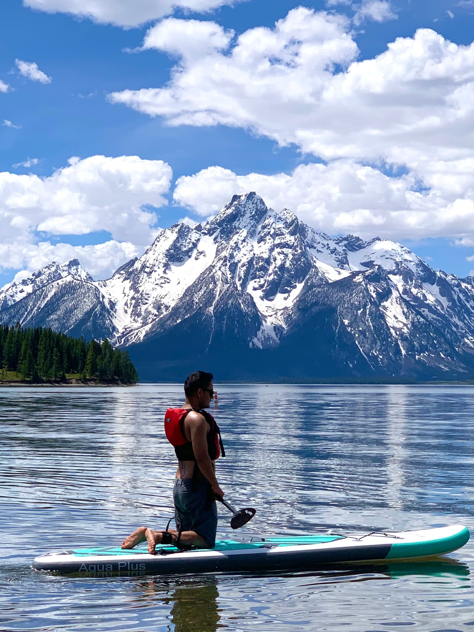 Nitesh kneeling on a paddleboard with snowy mountains rising across the lake